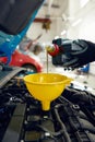 Man pouring engine oil into car motor through funnel