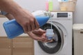 Man pouring fabric softener from bottle into cap near washing machine indoors, closeup Royalty Free Stock Photo