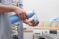 Man pouring fabric softener from bottle into cap near washing machine indoors, closeup Royalty Free Stock Photo