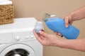 Man pouring fabric softener from bottle into cap near washing machine indoors, closeup Royalty Free Stock Photo