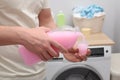 Man pouring fabric softener from bottle into cap near washing machine indoors, closeup Royalty Free Stock Photo