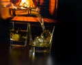 Man pouring glasses of whiskey with ice cubes in front of the fireplace