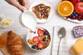 Man pouring greek yoghurt into granola at white wooden table, top view Royalty Free Stock Photo