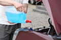Man pouring liquid from plastic canister into car washer fluid reservoir, c