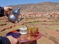 Man pouring mint tea into glasses on colorful tray, Ourika valley and High Atlas Mountains in the background. Morocco. Royalty Free Stock Photo