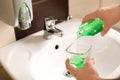 Man pouring mouthwash from bottle into glass in bathroom, closeup.