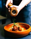 Man Pouring Pepper On Beef Cheeks In A bowl