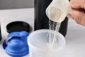 Man pouring protein powder from measuring scoop into shaker on white table Royalty Free Stock Photo