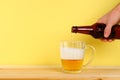 A man pours beer into a mug from a bottle on a yellow background on a wooden table. Copy space. Royalty Free Stock Photo