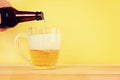 A man pours beer into a mug from a bottle on a yellow background on a wooden table. Copy space. Royalty Free Stock Photo