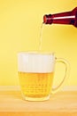 A man pours beer into a mug from a bottle on a yellow background on a wooden table. Copy space. Royalty Free Stock Photo