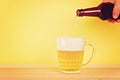 A man pours beer into a mug from a bottle on a yellow background on a wooden table. Copy space. Royalty Free Stock Photo
