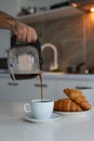 A man pours coffee from a coffee pot into a white cup, cozy kitchen