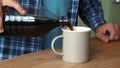 man pours cola into a mug while sitting in the kitchen