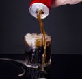 a man pours on a dark table past a glass full of ice soda from a red aluminum can. The drink is produced and manufactured by Royalty Free Stock Photo