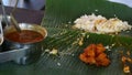 Man Pours out Dressings Onto Indian Food on Banana Leaf