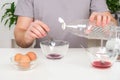 A man pours spoonful vinegar into glass cup with dye. Dyeing eggs with coloring in Easter egg