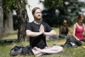 Man practicing yoga at the city park, group of people meditating on a background