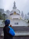 Man praying at buddhist shanti stupa covered with misty fog at morning from different angle