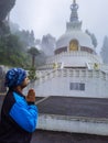 Man praying at buddhist shanti stupa covered with misty fog at morning from different angle