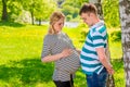 Man and pregnant woman compare their stomachs, shot in the park