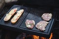 Man prepares a juicy pork neck with basil and barbecue spices and a baguette with tomato cheese and ham on a hot granite slab.