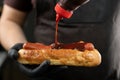 Man preparing a hot dog. Chef in gloves pours ketchup over a hot dog. Cooking fast food. Royalty Free Stock Photo