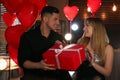 Man presenting gift to his girlfriend in room with heart shaped balloons. Valentine`s day celebration Royalty Free Stock Photo