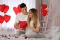 Man presenting gift to his girlfriend in room decorated with heart shaped balloons. Valentine`s day celebration Royalty Free Stock Photo