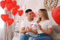 Man presenting gift to his girlfriend in room decorated with heart shaped balloons. Valentine`s day celebration Royalty Free Stock Photo