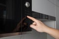 A man presses his finger on the touch panel of a microwave oven to turn on the defrost function. High tech modern microwave oven