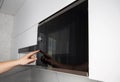 A man presses his finger on the touch panel of a microwave oven to turn on the defrost function. High tech modern microwave oven