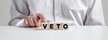 Man pressing his finger on the wooden cubes with the word veto. Veto power in politics or business