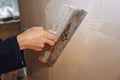 Man is priming a surface with a palett knife. Maintenance repair works renovation in the flat. Restoration indoors. Concrete