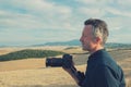 Man professional photographer with digital camera walking in tuscany fields and taking photos. Photo Camera in male hands over Royalty Free Stock Photo