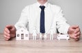 Man protecting figures of family, car and house at wooden table. closeup. Insurance concept Royalty Free Stock Photo