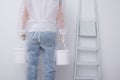 A man in protective clothing, bringing buckets of paint, against the background of a white wall and a stepladder, rear view Royalty Free Stock Photo