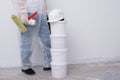 A man in protective clothing, with paint rollers in his hands, put four buckets on top of each other, against the background of a Royalty Free Stock Photo