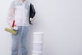 A man in protective clothing, with paint rollers in his hands, put three buckets on top of each other, against the background of a Royalty Free Stock Photo