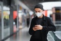 Man in protective mask with cell phone at a shopping centre or underground.