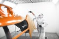 Man in protective mask and clothes sprays varnish to car hood with a spray gun in a paint booth. Royalty Free Stock Photo