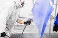 Man in protective mask and clothes sprays varnish to hood of car with a spray gun in a paint booth. Royalty Free Stock Photo