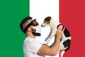 Man in protective mask and glasses with dog wearing face mask and abstract virus strain on Italian flag Royalty Free Stock Photo