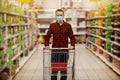 Man in protective mask shopping in supermarket pushing trolley during epidemic