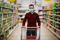 Man in protective mask shopping in supermarket pushing trolley during epidemic