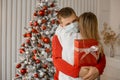 Man in protective medical mask looking at camera and hugging his woman holding a gift at her back near christmas tree. Isolation Royalty Free Stock Photo