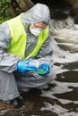 A man in a protective suit holds a Petri dish with a sample for plants and looks at the reaction in it after adding the reagent