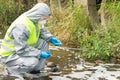 A man in a protective suit holds a Petri dish with a sample for plants and looks at the reaction in it after adding the reagent,