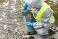 A man in a protective suit holds a Petri dish with a sample for plants and looks at the reaction in it after adding the reagent,