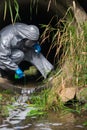 A man in a protective suit and mask in a large sewer pours reagent from a flask for wastewater treatment